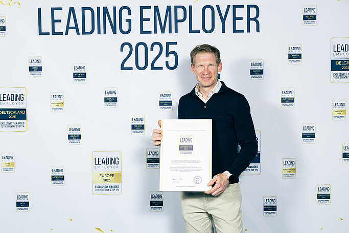 CEO Philipp Pfaller mit der Auszeichnung Leading Employer 2025 vor der Interview-Wand