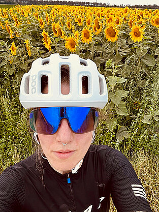 Beate am Rennrad vor einem Sonnenblumenfeld.